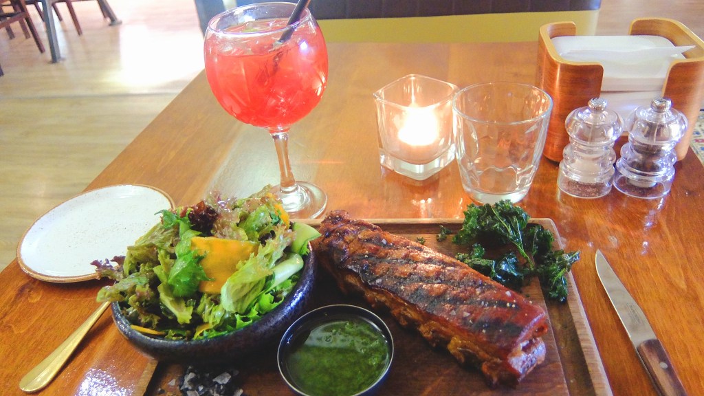 Restaurangportion med revbensspjäll av fläskkött, fräsch sallad och knaperstekt grönkål, alkoholfri dryck