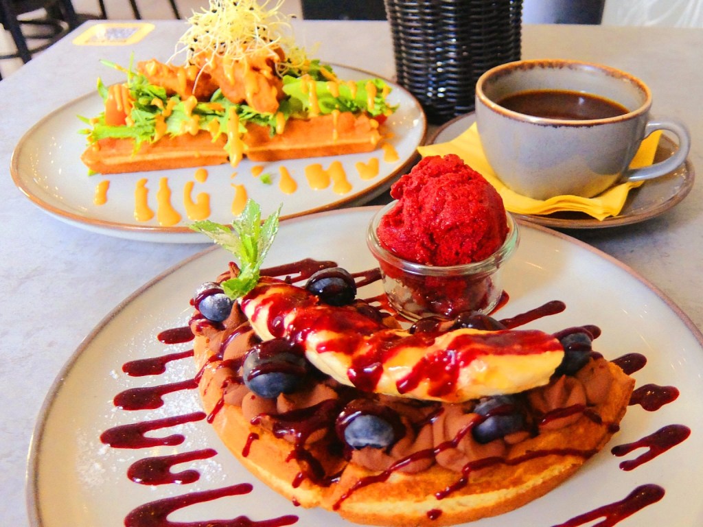 A coffee table at a gluten-free waffles cafeteria showing two yummy dishes and a cup of coffee