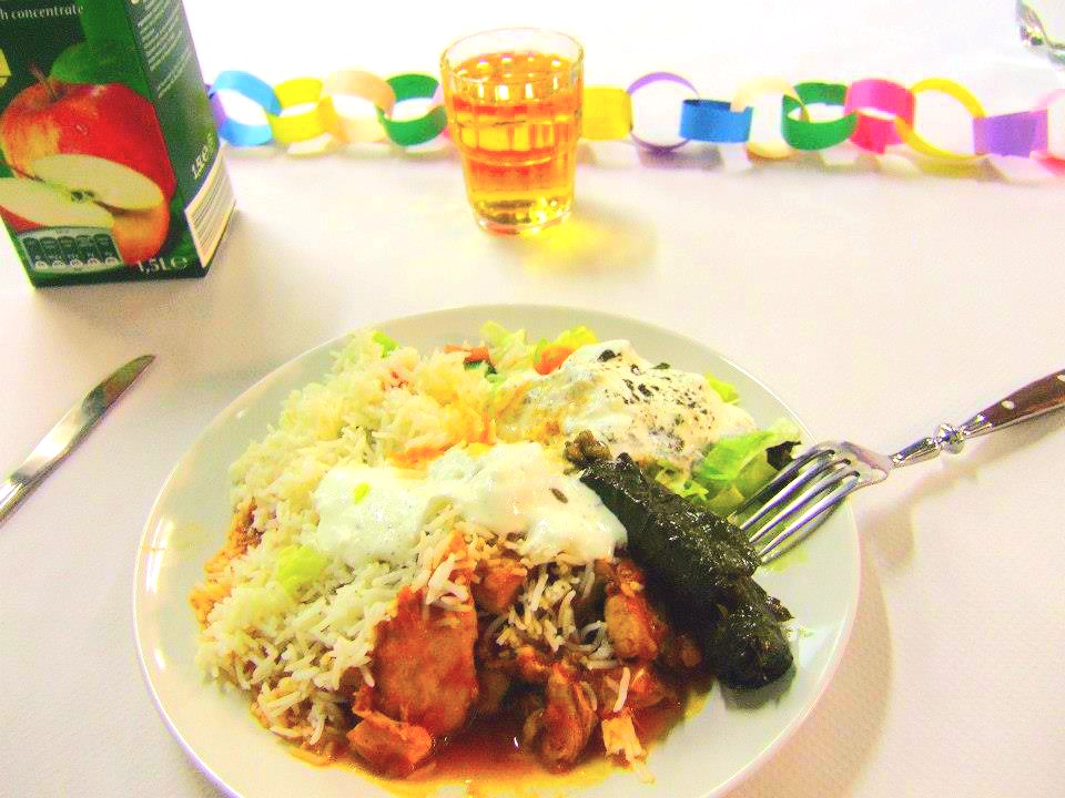 A plate with a rise and meat-dish looking yummy and a glass of apple juice on a festive occasion